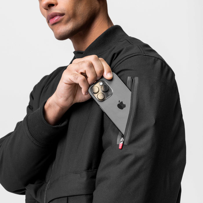 Kinterra Weatherproof Bomber Jacket in black, worn by model holding smartphone in jacket pocket