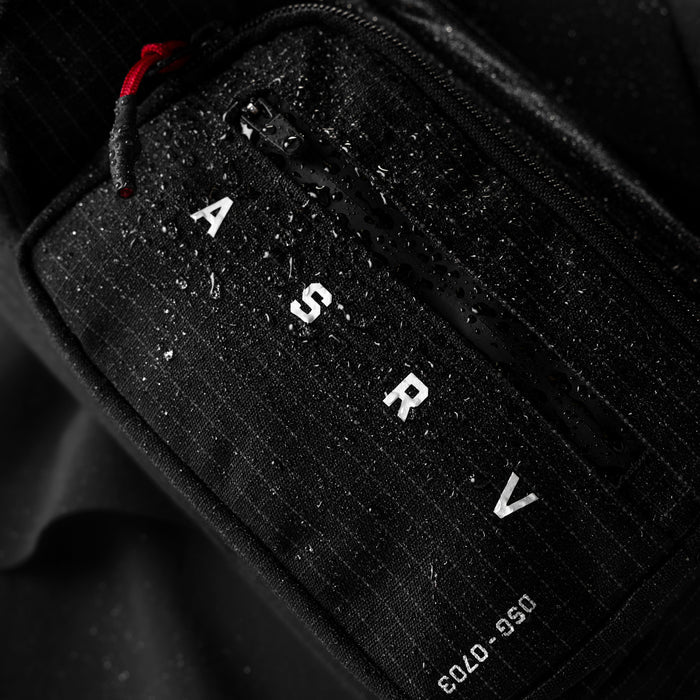 0703 Cordura Tech Crossbody Pack in black grid, carried with red zipper pull visible