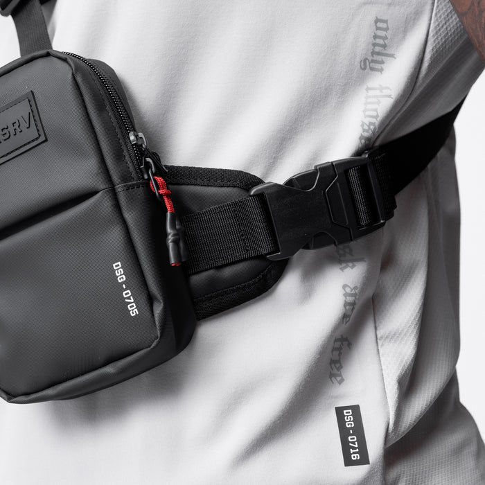 Black waterproof holster sling bag worn across chest on model in white athletic jacket