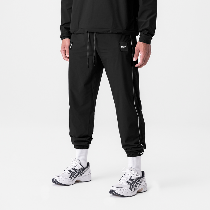 Black ripstop oversized track pants with side stripe worn with white socks and sneakers, front view