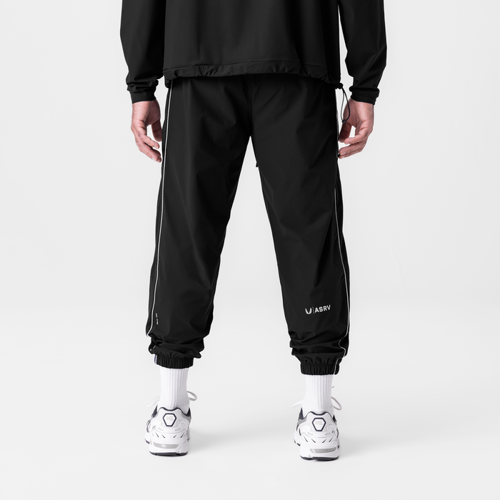 Black ripstop oversized track pants with side stripe, back view on model wearing white socks and sneakers