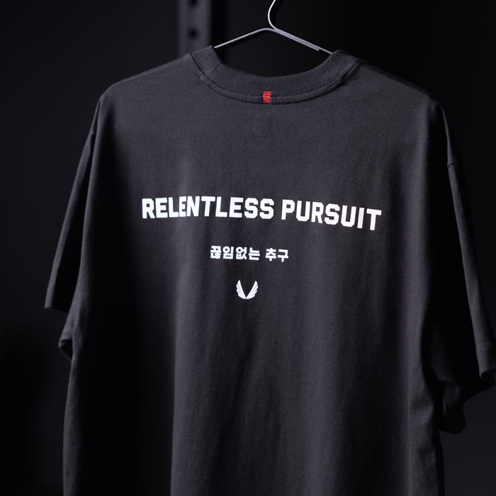 Black 'Relentless Pursuit' relaxed tee on hanger, front view showing graphic print and Korean text