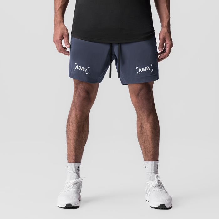 Navy Tetra-Lite 7" linerless shorts with bracket logo, worn by model with white sneakers