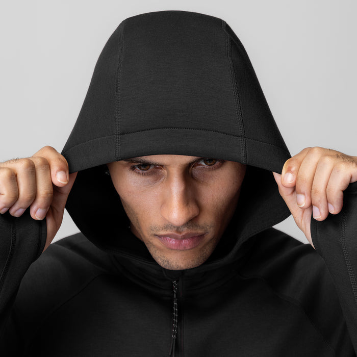 Black Dri-Core™ Zip Hoodie worn by model pulling hood over head, front view