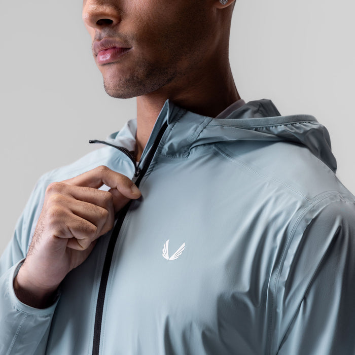 Aerotex Lightweight Windbreaker in light sky, worn by model holding hood drawstring