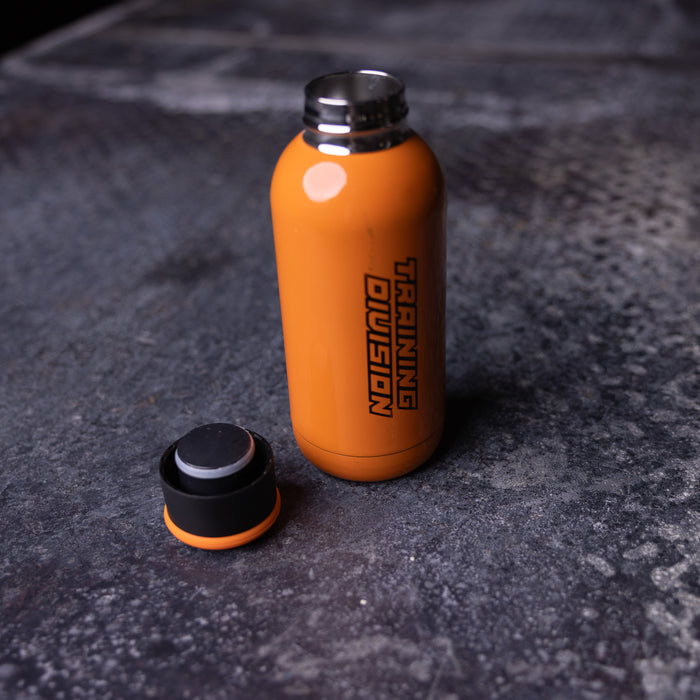flatlay of ASRV Training Division water bottle in orange with black cap, shot from above on concrete surface
