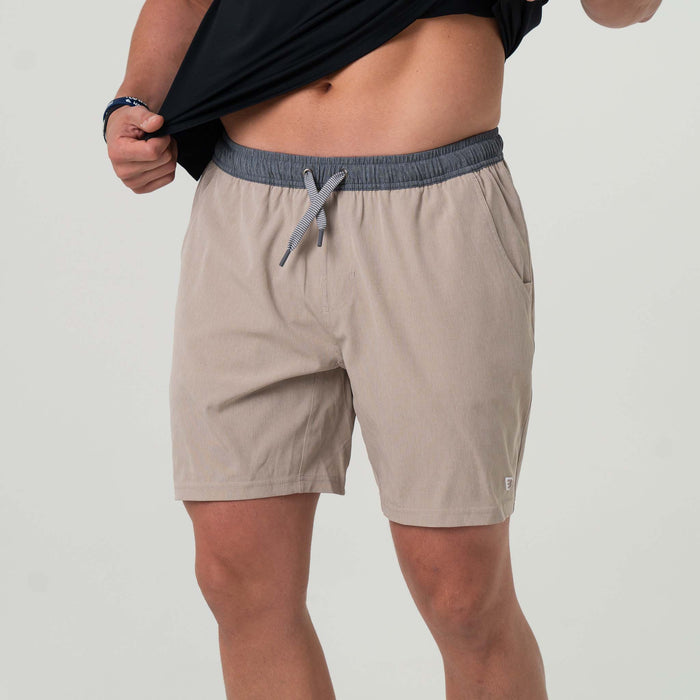 Waist to knee view of man wearing beige athletic shorts that have  grey waistband and a drawstring closure.