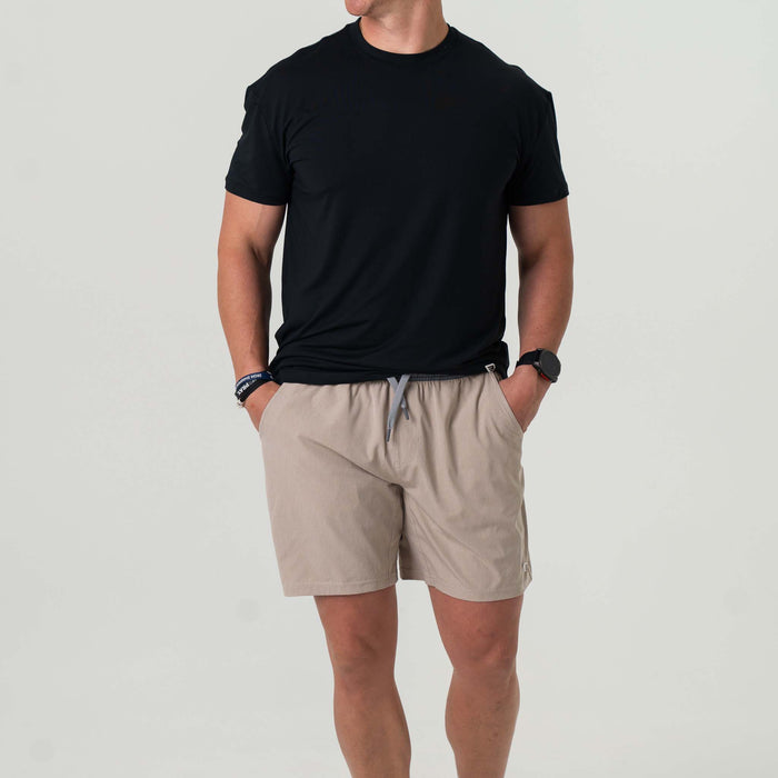 Front view of man wearing beige athletic shorts. He has his hands in his pockets.