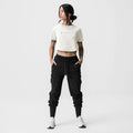 ASRV x Tonal Women's AeroSilver® Cropped Training Tee in ivory cream, worn with black cargo joggers
