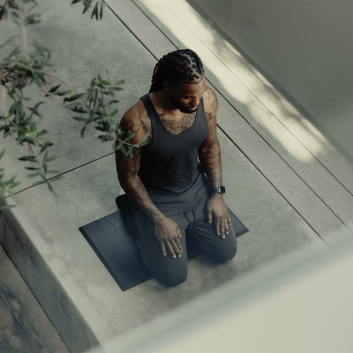 Man wearing black ASRV meditation bench outfit, kneeling on mat in minimalist space