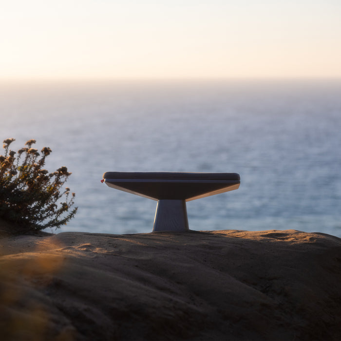 ASRV x Walden Meditation Bench in black, displayed on rocky coastal landscape at sunset