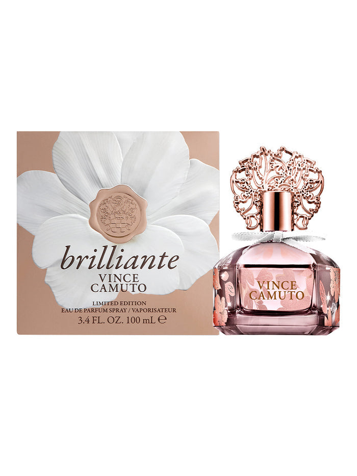 A bottle of Vince Camuto Brilliante 3.4 oz Eau de Parfum Spray is displayed before its box, adorned with a large white flower and elegant script. The bottle features a pink hue and an ornate rose gold cap, capturing the essence of this sparkling scent with radiant white florals—an irresistible fragrance for women.