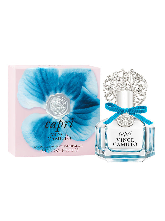 A 3.4 oz bottle of Capri Eau de Parfum Spray by Vince Camuto, adorned with a decorative silver cap and blue ribbon, is displayed beside its pink box featuring a large blue flower and branded detailing—perfectly capturing the essence of its floral fruity fragrance with a sparkling citrus blend.