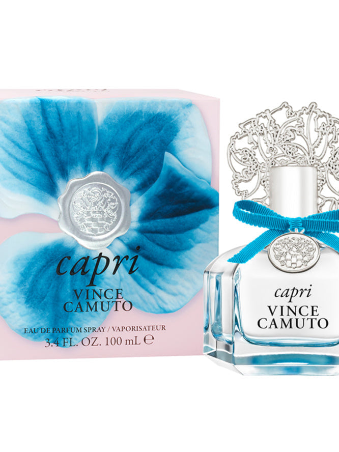 A 3.4 oz bottle of Capri Eau de Parfum Spray by Vince Camuto, featuring an ornate silver cap and a blue ribbon, is displayed beside its box adorned with blue petals and silver accents. This elegant fragrance captivates the senses with a fresh citrus blend and a radiant floral fruity scent.