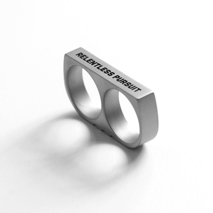 flatlay Double Ring stainless steel knuckle ring with "Relentless Pursuit" engraving, silver, angled view
