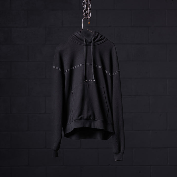 Black contrast thread hoodie displayed on hanger against dark brick wall