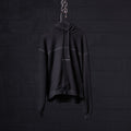 Black contrast thread hoodie displayed on hanger against dark brick wall