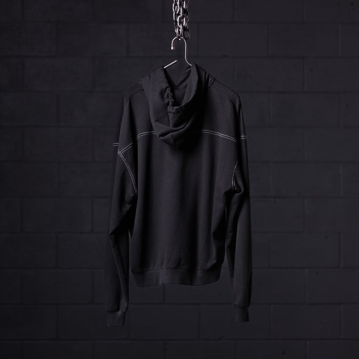 Black contrast thread hoodie displayed on hanger against dark brick wall background
