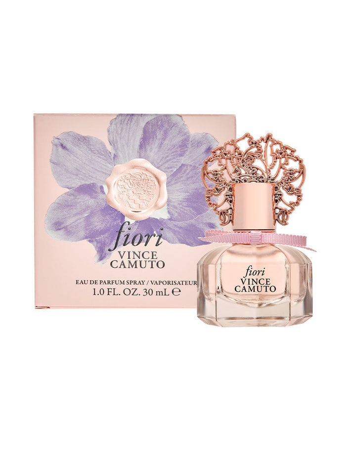 A bottle of Fiori 1.0 oz Eau de Parfum Spray by Vince Camuto, adorned with a decorative rose gold cap, is displayed in front of its box, which features a large purple flower design and the product name.