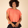 Free People Movement My Time Tee in Neon Coral, sizes XS–XL. Front view of model smiling in the boxy cropped tee with wide sleeves and soft crew neckline.