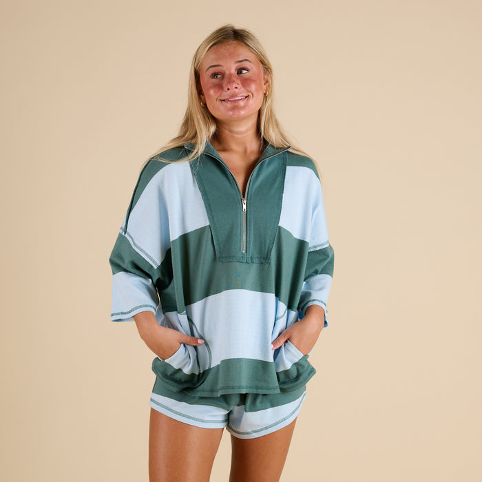 Model wearing FP Movement Retro Rugby Set in Heritage Green Combo, featuring an oversized half-zip striped top with pockets and matching striped shorts.