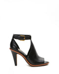 The Vince Camuto Frasper Shootie is a black leather high-heeled peep-toe sandal with an open toe, cutout design, and gold buckle ankle strap, featuring a cushioned footbed for added comfort, shown in side profile on a white background.
