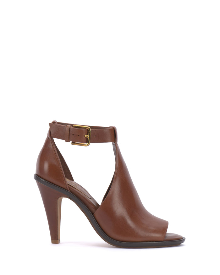 The Vince Camuto Frasper Shootie is a brown leather T-strap sandal with high heels, featuring a closed heel, open toe, ankle strap with a gold buckle, and a cushioned footbed for enhanced comfort. Displayed in profile against a white background.