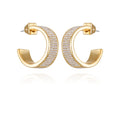 The Vince Camuto Goldtone Crystal C Hoop Earrings showcase a thick band adorned with rows of shimmering crystals along the outer surface, beautifully displayed on a white background with a mirrored reflection beneath—these modern earrings lend sophisticated style to any ensemble.
