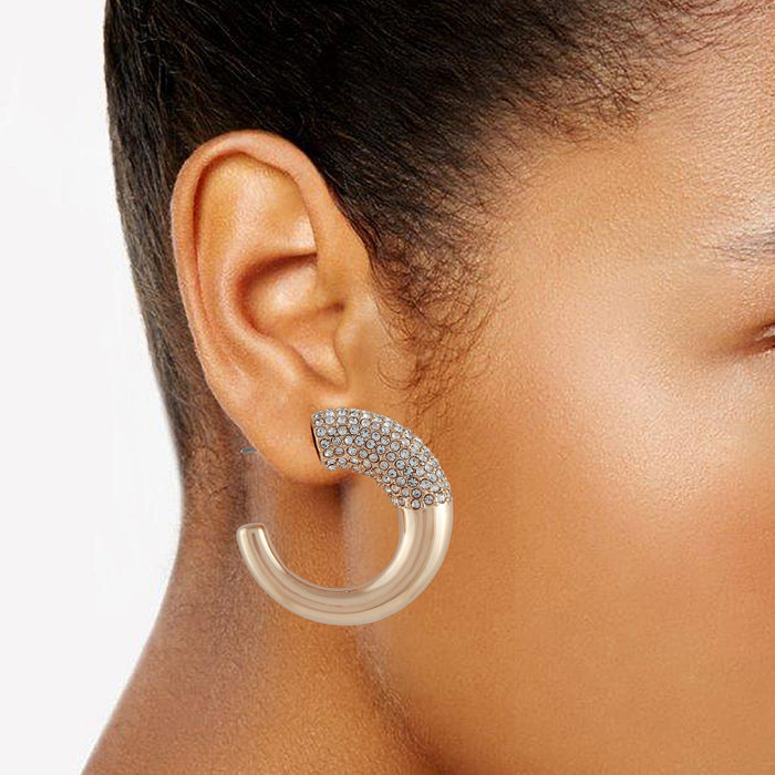 A close-up of a person’s ear, with medium brown skin tone, wearing the Vince Camuto Goldtone Pave Crystal Stone Open Hoop Earring. The large, semi-circular goldtone hoop features sparkling pave crystals along the upper section and is set against a white background.