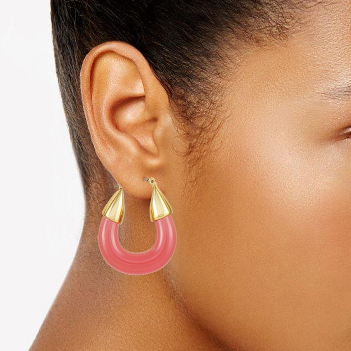 A close-up of a woman’s ear wearing Vince Camuto Goldtone Pink Candy Hoop Earrings. The large, pink resin hoops with gold accents are in sharp focus against a plain background.