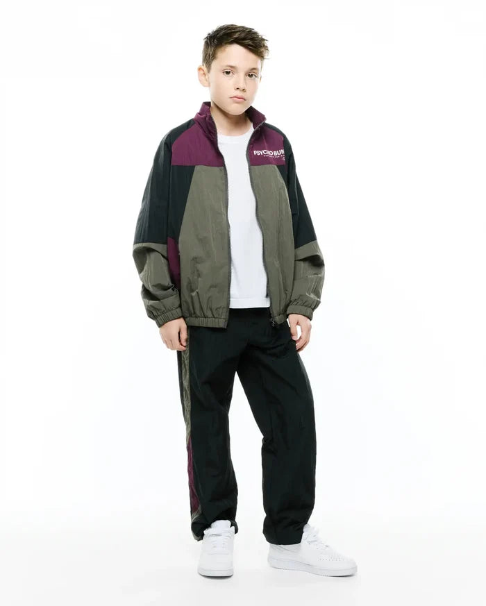 Kids Alder Nylon Colorblock Jacket in black, olive green, and deep plum, featuring a relaxed fit, full zip, and small white Psycho Bunny text logo on the left chest, paired with matching track pants.