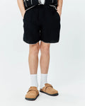 Kids Brad Linen Short, black relaxed fit linen shorts with elastic waistband, white contrast stitching on hem, and a subtle embroidered Psycho Bunny skull logo on the lower left leg.