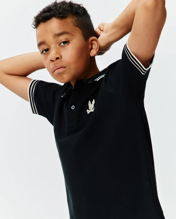 Kids Brad Pique Polo, a classic black pique polo shirt with a two-button placket, ribbed collar, and double white striped sleeve cuffs, featuring a small embroidered silver Psycho Bunny skull logo on the left chest.