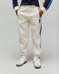 Kids Caspian Contrast Stripe Track Pant in cream french terry, featuring a relaxed fit, dark blue side stripe, and a small embroidered Psycho Bunny skull logo on the left thigh.
