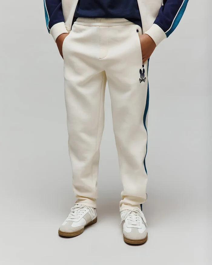 Kids Caspian Contrast Stripe Track Pant in cream french terry, featuring a relaxed fit, dark blue side stripe, and a small embroidered Psycho Bunny skull logo on the left thigh.