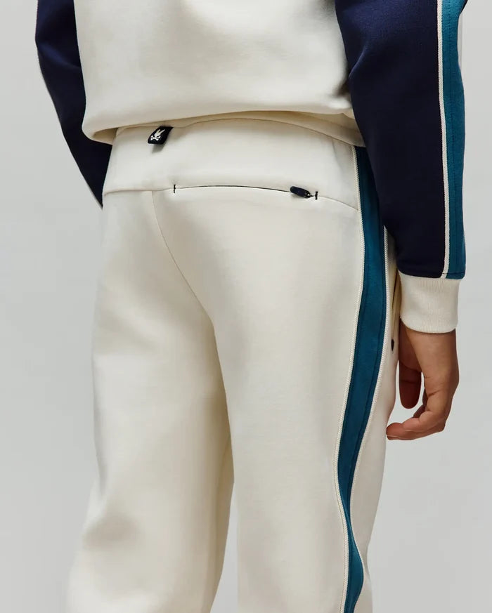 Kids Caspian Contrast Stripe Track Pant in cream french terry, featuring a relaxed fit, teal and white side stripes, a small Psycho Bunny logo tag on the waistband, and a zippered back pocket.