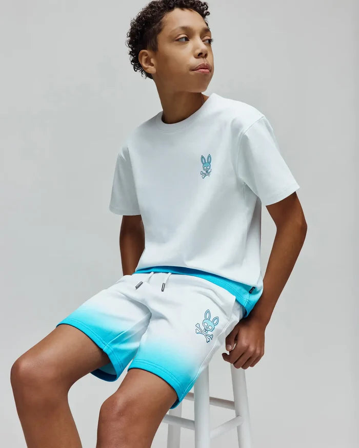 White jersey t-shirt with small blue embroidered Psycho Bunny skull logo on chest, paired with Kids Dax Sweatshort featuring white to blue ombre design, relaxed fit, and large blue embroidered bunny skull logo on thigh.