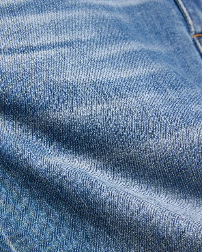 Kids Emerson Denim Pant featuring a classic medium blue washed denim with a prominent twill weave texture, natural fading, and subtle creasing, accented by visible warm brown stitching.