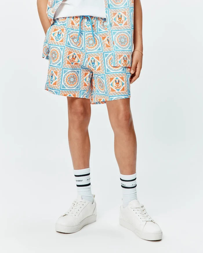 Kids Frank Swim Trunk in white with a vibrant blue and orange mosaic pattern, featuring repeated Psycho Bunny skull logos and a bright blue drawstring, in a relaxed fit.