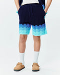 Kids Holden Knit Short in navy blue with a relaxed fit, featuring a wavy gradient pattern in light blue and aqua, textured knit fabric, and a small embroidered Psycho Bunny skull logo on the left leg.