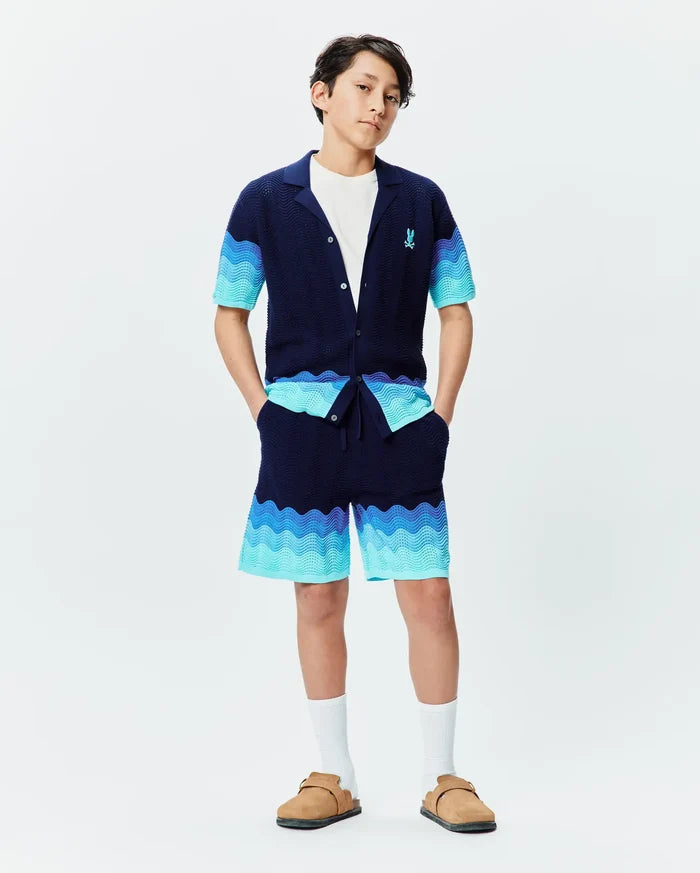 Psycho Bunny navy knit collared shirt and Kids Holden Knit Short set, featuring a wavy gradient pattern in blues and turquoise, textured knit fabric, and a small embroidered blue bunny skull logo on the left chest.
