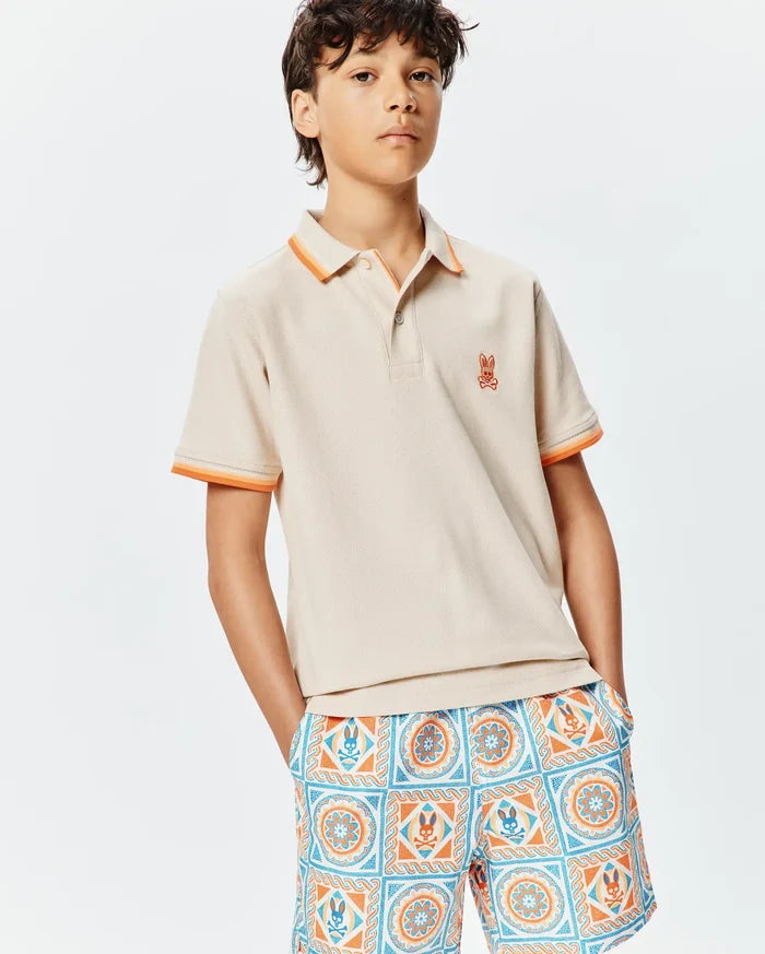 Kids Holden Pique Polo in beige, classic fit, with orange and light orange striped pique collar and cuffs, featuring a small embroidered orange Psycho Bunny skull logo on the left chest.