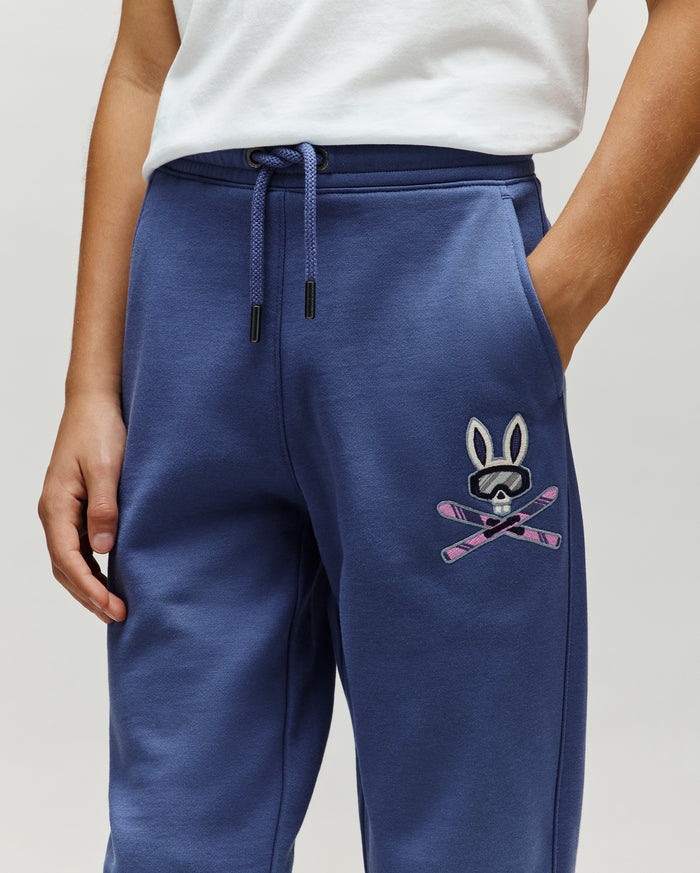Kids Indigo Ski Bunny Sweatpant, relaxed fit, made from soft french terry, features a medium-sized embroidered Psycho Bunny skull with ski goggles and crossed pink skis on the left thigh.