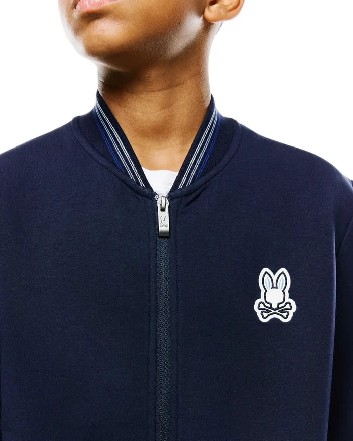 Kids Jaydon Track Jacket, navy smooth jersey, classic fit, full-zip with branded pull, ribbed collar with white and blue stripes, and an embroidered white and light blue Psycho Bunny skull logo on the left chest.