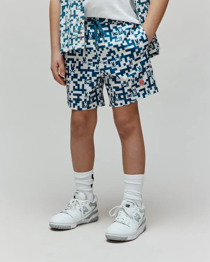 Kids Josh Swim Trunk, white with a deep blue pixelated pattern of repeating Psycho Bunny skull logos, a prominent red bunny logo on the right leg, and a relaxed fit in quick-dry fabric.