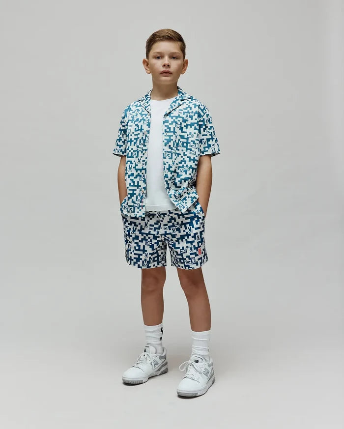 Kids Josh Swim Trunk and matching short-sleeve button-up shirt in a white and teal pixelated pattern featuring the Psycho Bunny skull logo, with a small red logo on the trunk, all in a relaxed fit.
