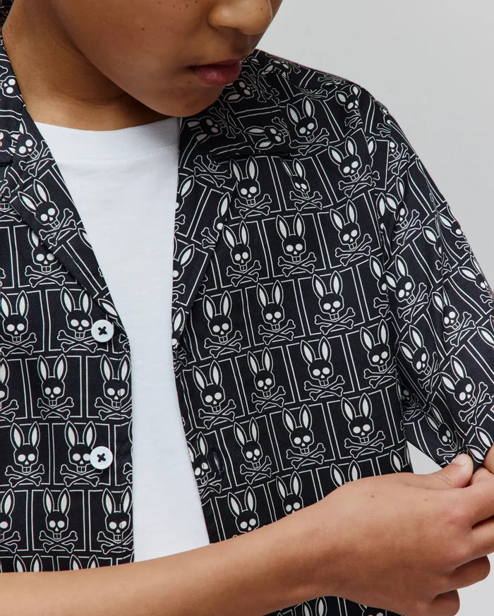 Kids Keon Tencel Shirt in black with an all-over white Psycho Bunny skull and crossbones logo pattern, featuring a relaxed fit, smooth Tencel fabric, and white buttons.
