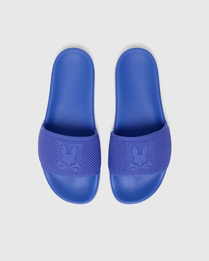 Kids Knit Slides in vibrant royal blue, featuring a comfortable textured sole and a wide knitted strap with a prominent woven Psycho Bunny skull logo.