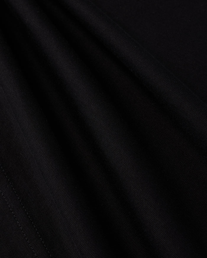 A close-up view of the smooth, dark fabric of the KIDS LOS ANGELES CITY TEE - B0U861A2PC by Psycho Bunny shows a fine, consistent weave. The folds create subtle shadows and highlights, accentuating the texture and soft appearance of this luxurious Peruvian Pima cotton material, suggesting it is well-crafted and of high quality.