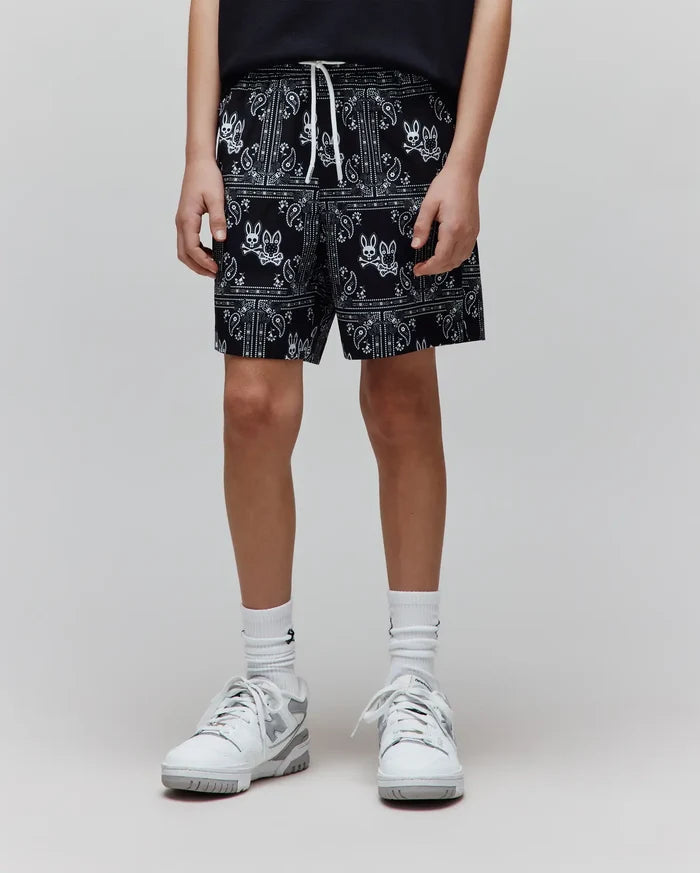 Kids Luke Swim Trunk in black with an all-over white bandana print featuring the Psycho Bunny skull logo, relaxed fit, and white drawstring.